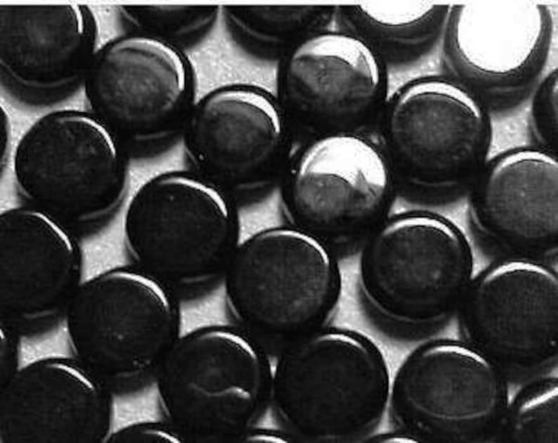 May include: A close-up image of a group of black round glass tiles. The tiles are smooth and shiny, and they are arranged in a random pattern.