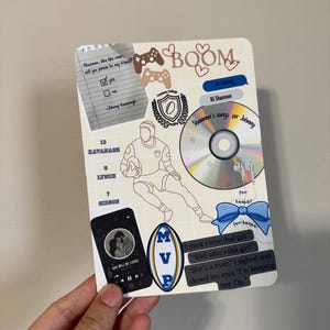 May include: A rectangular card with various stickers and text. Stickers include a rugby player, a CD, a phone with a music player, and a blue bow. Text includes "Shannon's songs for Johnny" and "She will be loved".