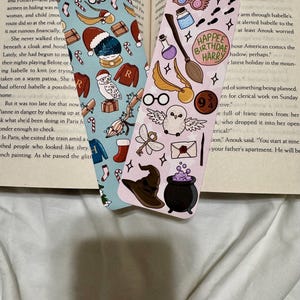 May include: Two decorative bookmarks with colorful illustrations. One features holiday-themed designs like a Santa hat and candy canes. The other has a magical theme with a broom, glasses, and the text "Happee Birthdae Harry".