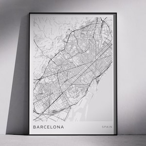 May include: A framed black and white map print of Barcelona, Spain. The detailed city map shows streets, buildings, and surrounding areas. The city name and country are printed at the bottom of the print.