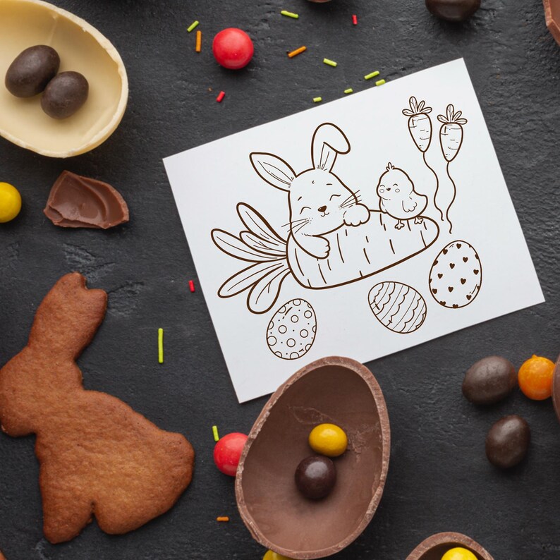May include: An overhead shot features Easter-themed treats and a drawing. The drawing depicts a bunny and chick on a carrot, with Easter eggs and carrots. Chocolate eggs, candies, and a bunny-shaped cookie are scattered on a dark surface.