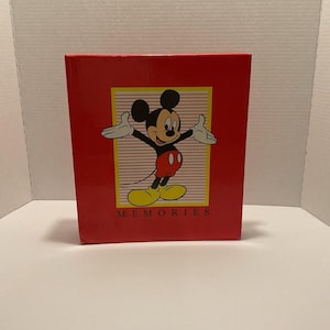 May include: Red photo album featuring Mickey Mouse with outstretched arms. The album has a yellow and black border with the word "MEMORIES" at the bottom. The album is a classic Disney collectible.