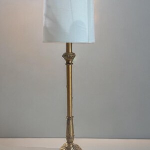 May include: A gold table lamp with a white drum shade. The lamp has a decorative base with intricate details.