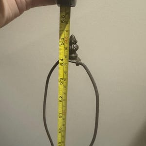 May include: A close-up of a lamp base with a metal harp and a decorative finial. The base is being measured with a tape measure, which reads 56 inches.