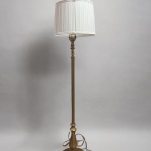 May include: A gold floor lamp with a white pleated lampshade. The lamp has a simple design with a round base and a tall, slender stem.