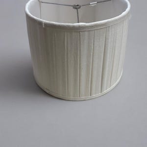 May include: A white pleated lampshade with a metal frame.