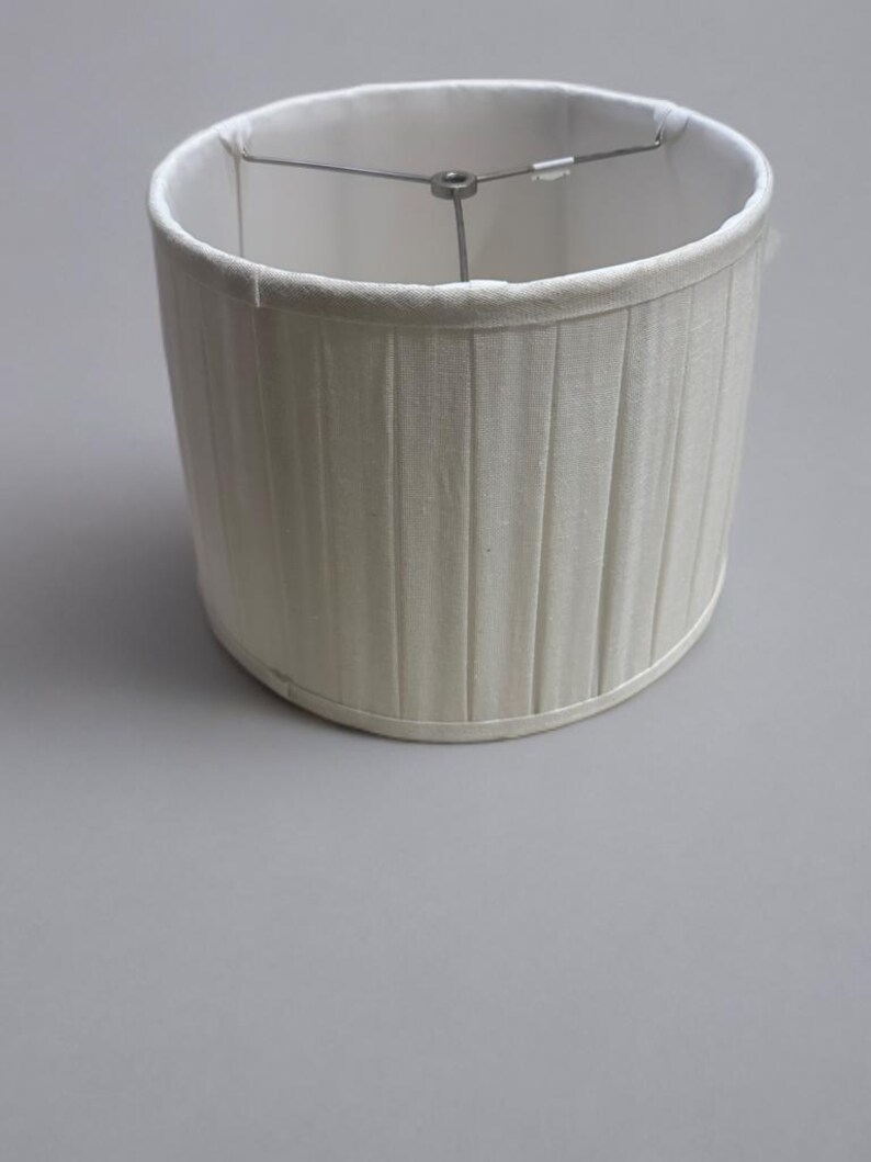 May include: A white pleated lampshade with a metal frame.