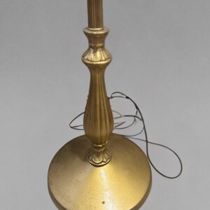 May include: A gold floor lamp with a decorative base and a simple, straight pole. The lamp is turned off and the cord is visible.