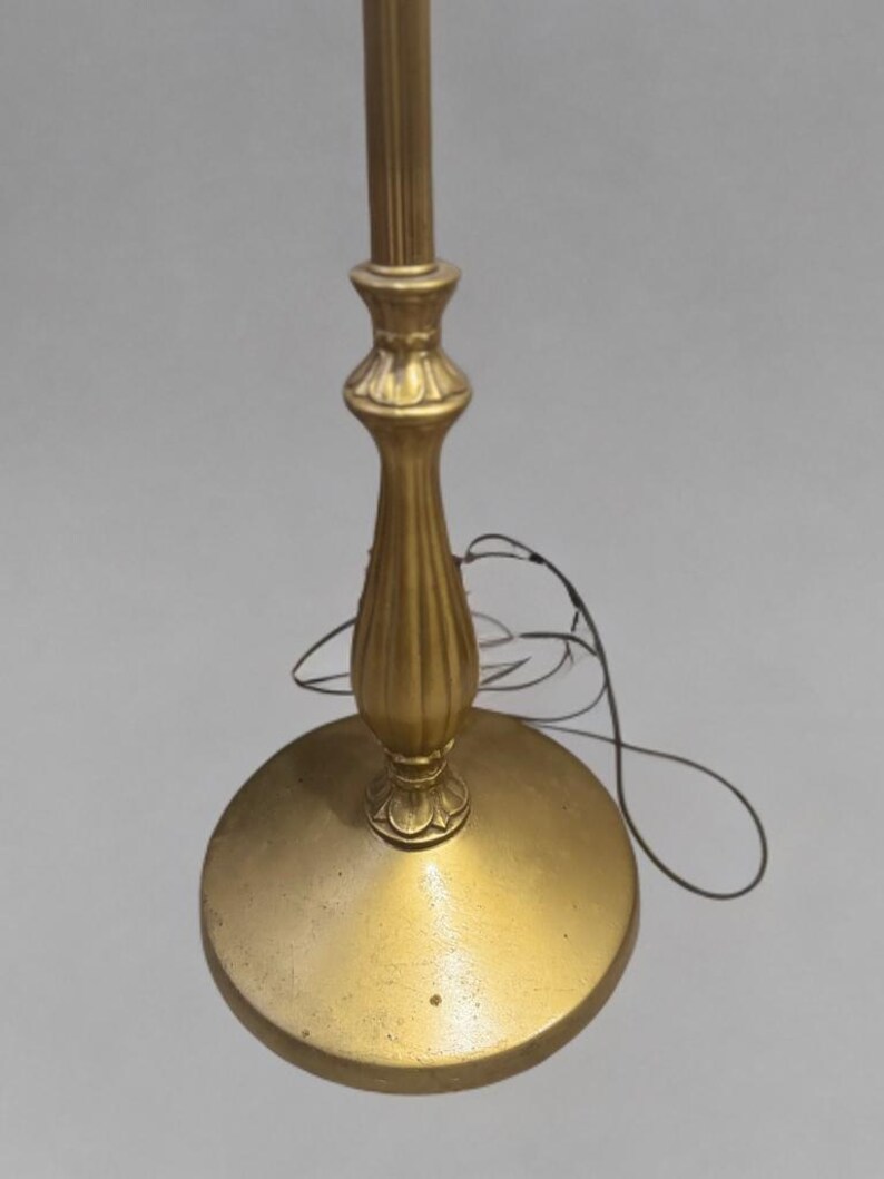 May include: A gold floor lamp with a decorative base and a simple, straight pole. The lamp is turned off and the cord is visible.