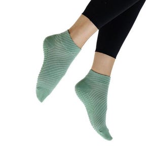May include: Light green ankle socks with a textured, non-slip sole. The socks feature a ribbed pattern and are worn with black leggings. These socks are designed for comfort and grip during activities like yoga or Pilates.