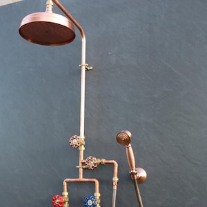 May include: Copper shower head with a handheld shower head and three valves. The shower head is mounted on a copper pipe.