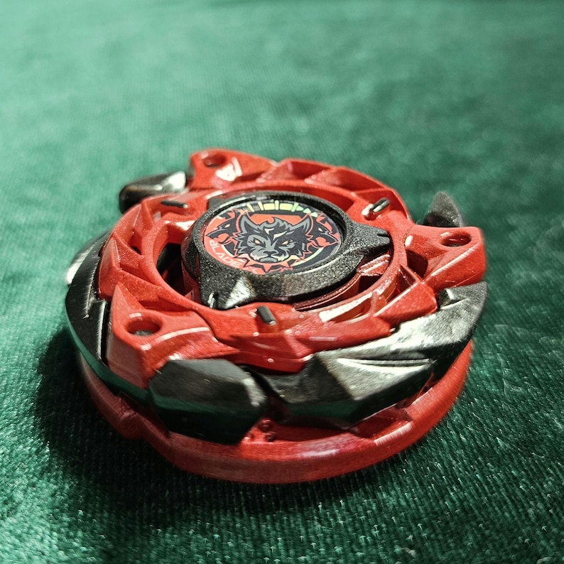 Puede incluir: Un juguete giratorio rojo y negro con un emblema de lobo en el centro. El juguete tiene un dise&ntilde;o multicapa con bordes afilados y una forma circular. La pieza central es negra con un gr&aacute;fico de lobo rojo.