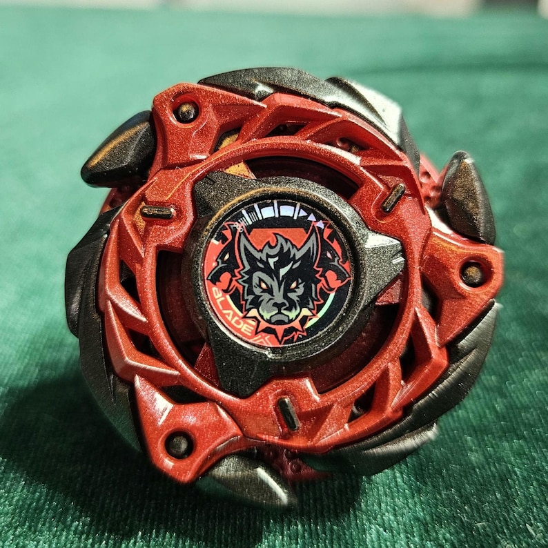 Puede incluir: Un juguete giratorio rojo y negro con un gr&aacute;fico de lobo en el centro. El juguete tiene un dise&ntilde;o multicapa con bordes afilados y una forma circular. El centro presenta la palabra "BLADE" y una ilustraci&oacute;n de lobo.