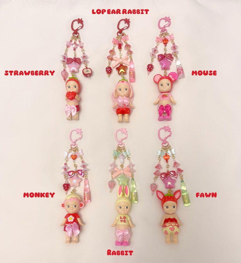 Pu&ograve; includere: Sei portachiavi con piccole bambole con accessori a tema animale. Ogni portachiavi ha una catena rosa o dorata con perline e ciondoli. Le figure sono vestite da fragola, topo, scimmia, coniglio e cerbiatto. Il testo sull'immagine recita "LOPEAR RABBIT".