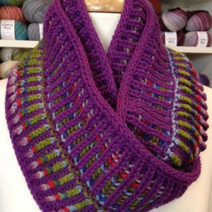 May include: A purple, green, blue, and red knitted infinity scarf with a textured pattern.
