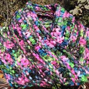 May include: A colorful knitted infinity scarf with a mix of pink, green, blue, and black yarn.