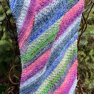 May include: A colourful striped knitted scarf in shades of pink, blue, green, and white. The scarf is folded and draped over a metal stand.