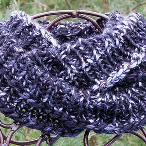 May include: A black and white knitted infinity scarf with a textured pattern. The scarf is displayed on a metal stand.