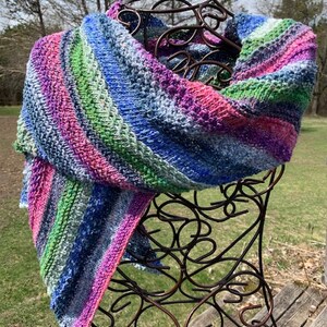 May include: A colourful striped knitted scarf in shades of blue, pink, green, and white. The scarf is draped over a decorative metal stand.