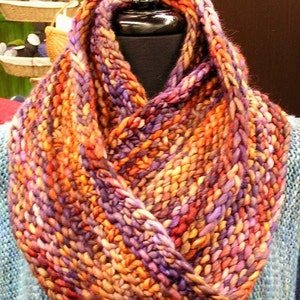 May include: A colorful knitted infinity scarf with a mix of orange, purple, and brown yarn. The scarf is folded in half and draped over a mannequin's neck.