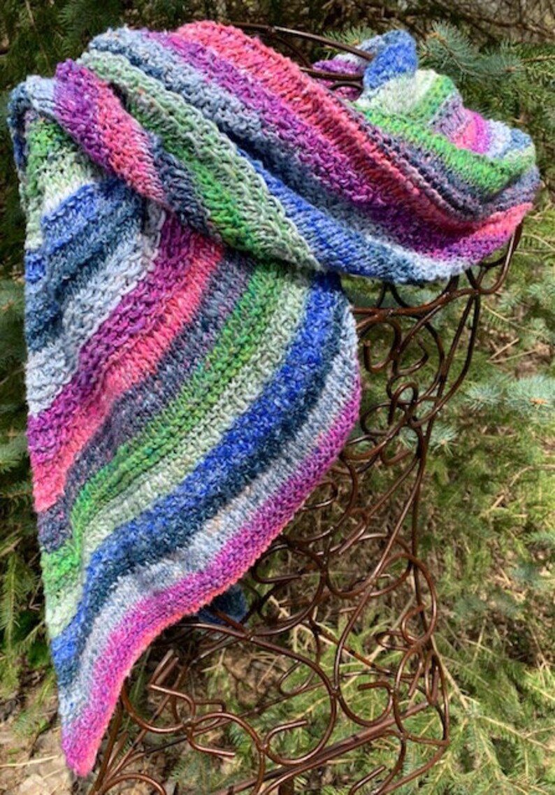 May include: A colourful striped knitted scarf in shades of pink, blue, green, and white. The scarf is draped over a brown metal stand.