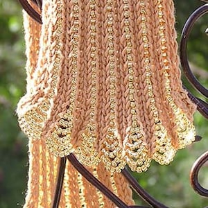 May include: A beige knitted scarf with a gold beaded trim. The scarf is draped over a metal stand.