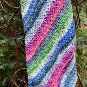 May include: A colourful striped knitted scarf with a diagonal pattern in shades of blue, green, pink, and white.