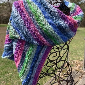May include: A colourful striped knitted scarf in shades of blue, green, pink, and purple. The scarf is draped over a wire mannequin.