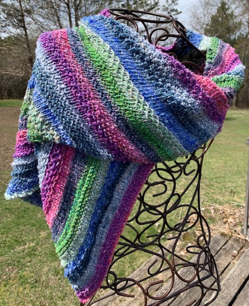 May include: A colourful striped knitted scarf in shades of blue, green, pink, and purple. The scarf is draped over a wire mannequin.