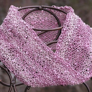May include: A pink and white crocheted cowl with a beaded design. The cowl is displayed on a metal stand.