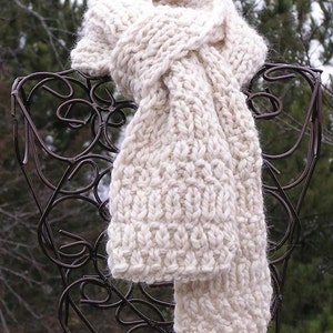 May include: A white knitted scarf with a chunky knit texture. The scarf is folded and draped over a metal stand.