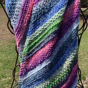 May include: A colourful striped knitted scarf with shades of blue, green, pink, and purple. The scarf is draped over a metal stand.