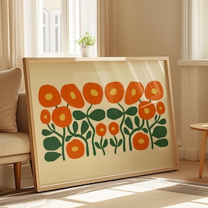 Può includere: Una stampa artistica incorniciata con un design floreale. La stampa presenta fiori arancioni con centri gialli e foglie verdi su uno sfondo color crema. L'opera d'arte è in una cornice di legno chiaro ed è appoggiata a un muro.