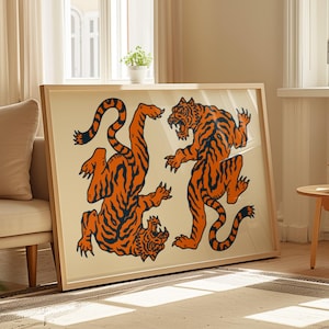 May include: A framed art print featuring two stylized tigers in orange and black. The tigers are depicted in dynamic poses against a cream-colored background. The artwork is encased in a light-colored wooden frame, suitable for home decor.