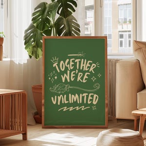 May include: A framed green poster with the words "TOGETHER WE'RE UNLIMITED" in a whimsical font. The poster has a brown wooden frame and is displayed in a well-lit living room setting. The image includes a large green plant and wooden furniture.
