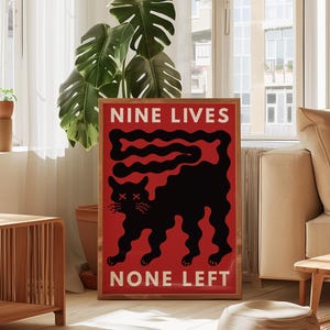 以下が含まれることがあります： 赤い背景に黒猫のイラストが描かれた額入りのアートプリント。「NINE LIVES」と「NONE LEFT」の文字は白。猫は長い尻尾とバツ印の目を持つ。リビングルームに飾られたアート作品。