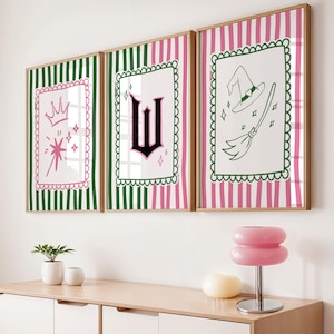 May include: Three framed art prints with whimsical illustrations. Each print features a white background with a different design: a crown and magic wand, a letter "W", and a witch's hat and broom. The frames have pink and green striped backgrounds.