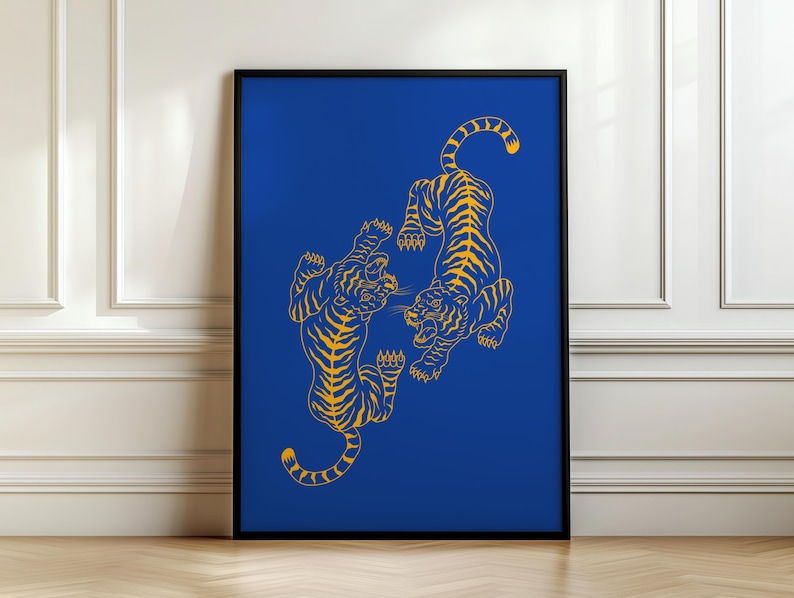 May include: A framed art print featuring two stylized yellow tigers on a vibrant blue background. The tigers are depicted in a dynamic pose, facing each other with open mouths and raised paws. The artwork is framed in a black border.