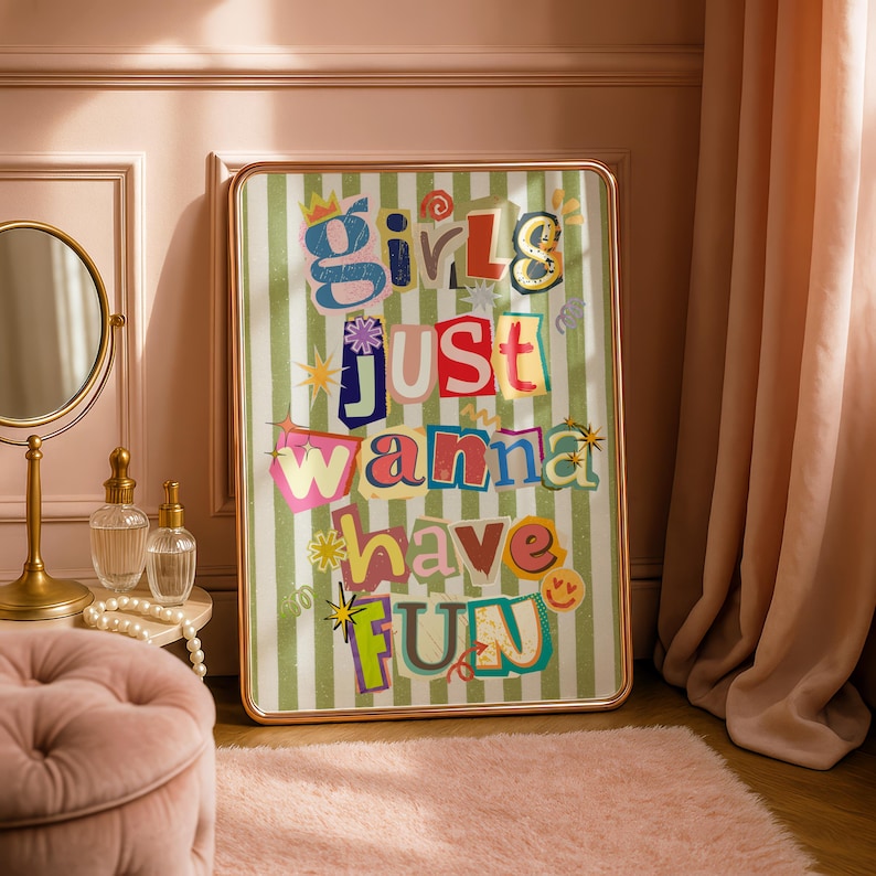 May include: A framed art print with the text "Girls Just Wanna Have Fun" in colorful, cut-out style letters. The background is a green and white striped pattern. The frame has a gold finish.