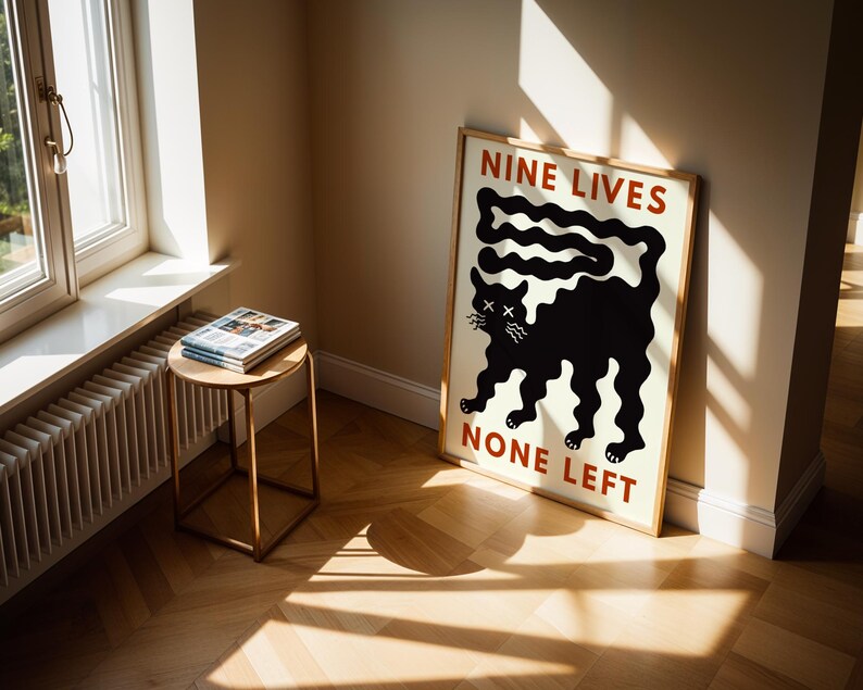 May include: A framed poster with a black cat illustration and the text "NINE LIVES NONE LEFT" in red. The poster is leaning against a wall in a room with a window and a small side table with magazines.