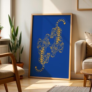 May include: A framed art print featuring two stylized yellow tigers on a vibrant blue background. The tigers are depicted in a dynamic pose, with intricate line work. The artwork is displayed in a room with natural light and wooden furniture.