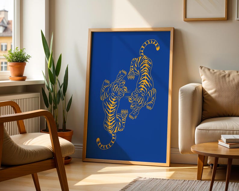 May include: A framed art print featuring two stylized yellow tigers on a vibrant blue background. The tigers are depicted in a dynamic pose, with intricate line work. The artwork is displayed in a room with natural light and wooden furniture.