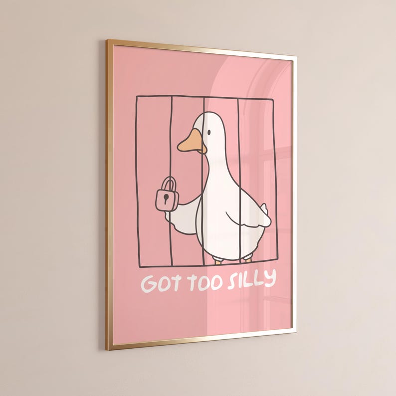 May include: Framed art print featuring a cartoon duck inside a cage, holding a padlock. The background is pink, and the text "GOT TOO SILLY" is at the bottom. The frame is gold.