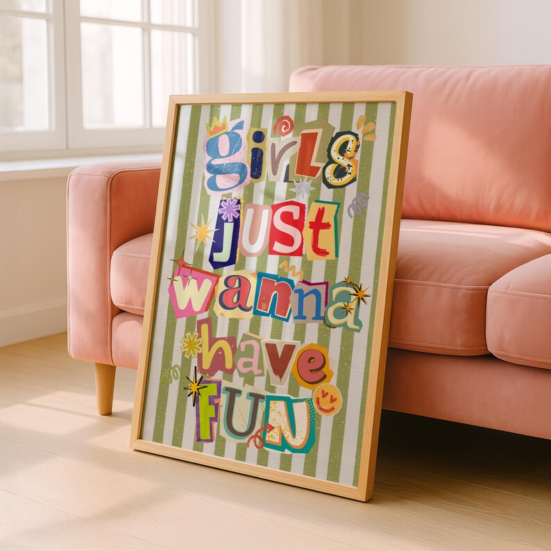 May include: A framed art print with the text "Girls Just Wanna Have Fun" in a colorful, collage-style design. The artwork features a light wood frame and a green and white striped background.