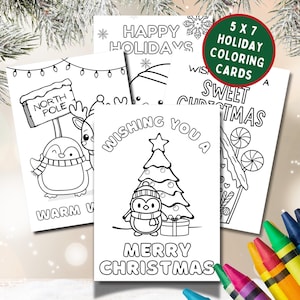 May include: A collection of 5x7 inch holiday coloring cards featuring festive designs. The cards include images of a penguin, reindeer, Christmas tree, and candy house, with text such as "Merry Christmas" and "Happy Holidays". Crayons are visible.