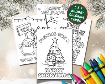 May include: A collection of 5x7 inch holiday coloring cards featuring festive designs. The cards include images of a penguin, reindeer, Christmas tree, and candy house, with text such as "Merry Christmas" and "Happy Holidays". Crayons are visible.