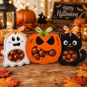 May include: Three felt Halloween treat holders shaped like a white ghost, an orange jack-o'-lantern, and a black cat. Each figure features a clear circular window filled with small orange-wrapped sweets and is topped with a decorative ribbon bow.