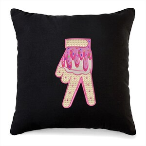May include: Black throw pillow with a pink and white embroidered hand making the peace sign. The hand is decorated with pink frosting and colorful sprinkles.