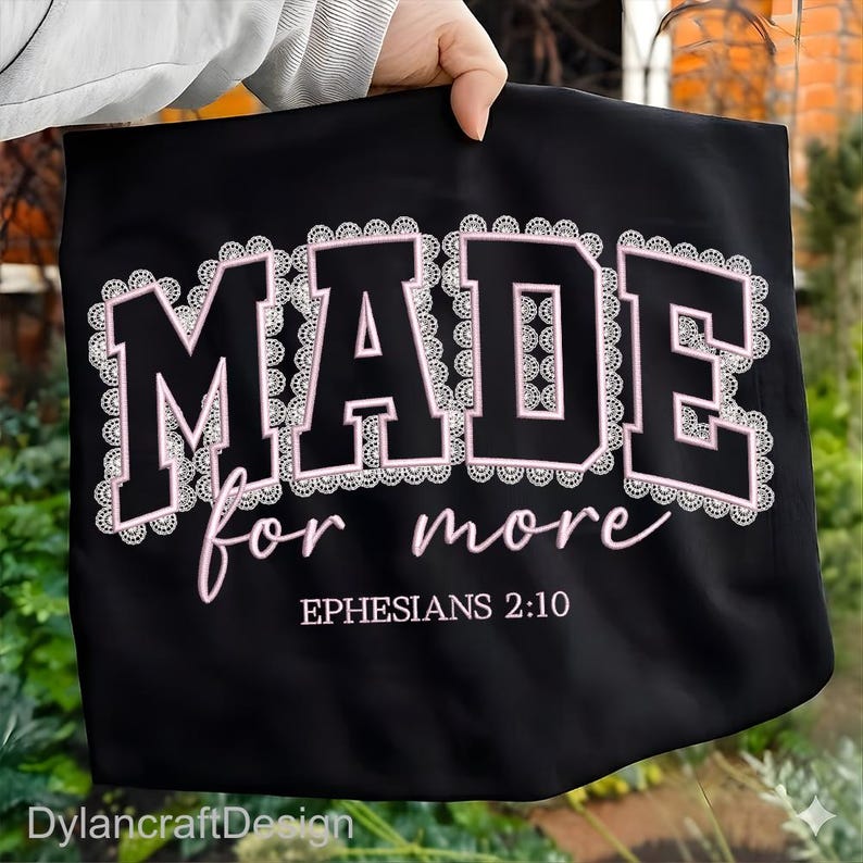 May include: Black tote bag featuring the text "MADE for more" in white and pink, with the reference "Ephesians 2:10" below. The bag is held by a person.