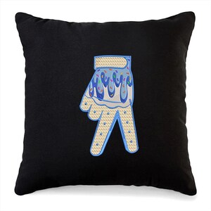 May include: A black pillow with a blue and white embroidered hand with sprinkles on top. The hand is making the peace sign.